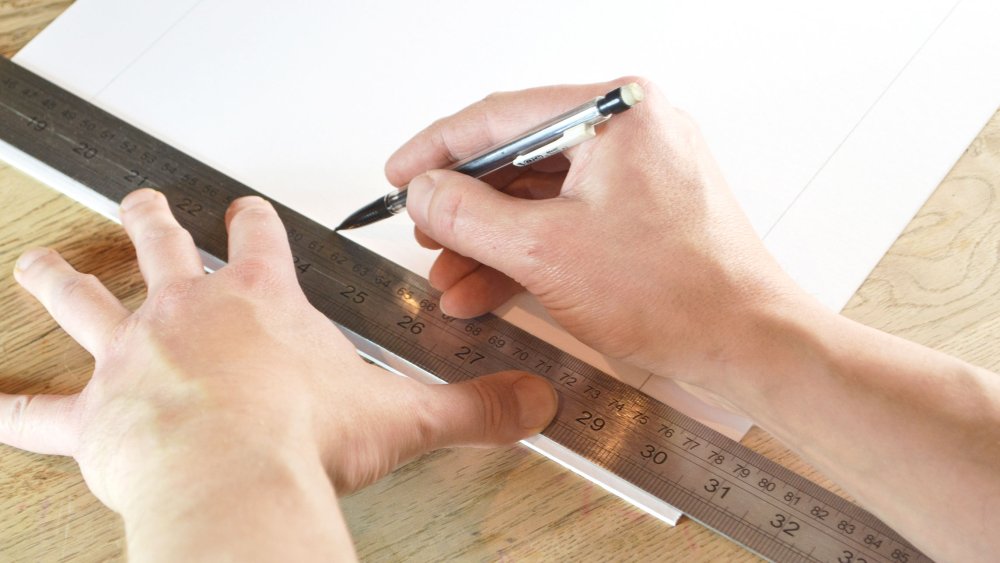 A person marking the aperture of a board with a pencil and ruler