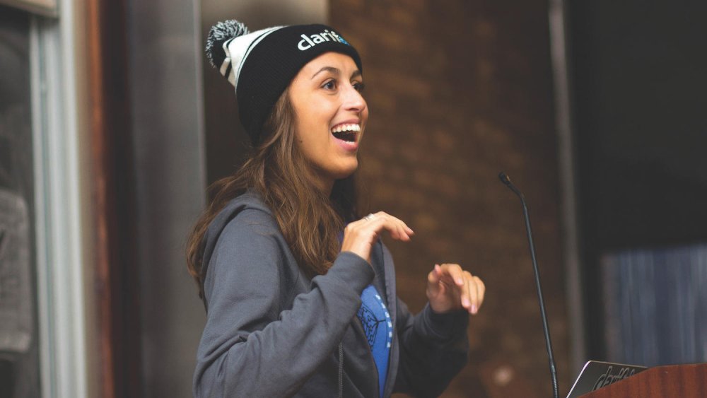 An image of Cassidy Williams speaking at a conference. She's stood at a podium, smiling and speaking to the audience downstage.