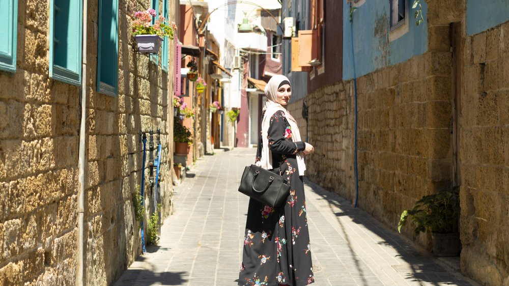 Generate speaker Sara Soueidan walks down a quiet street in Lebanon, looking back at the camera over one shoulder.