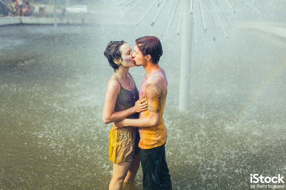 A couple in shorts and t-shirts stand in a fountain kissing