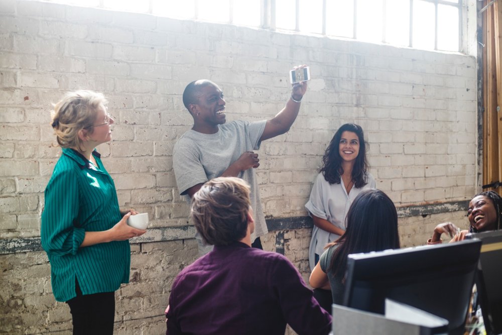 Man standing against a wall and laughing at his phone, along with a group of others