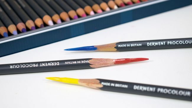 Three coloured Derwent Procolour pencils with the edge of the tin behind