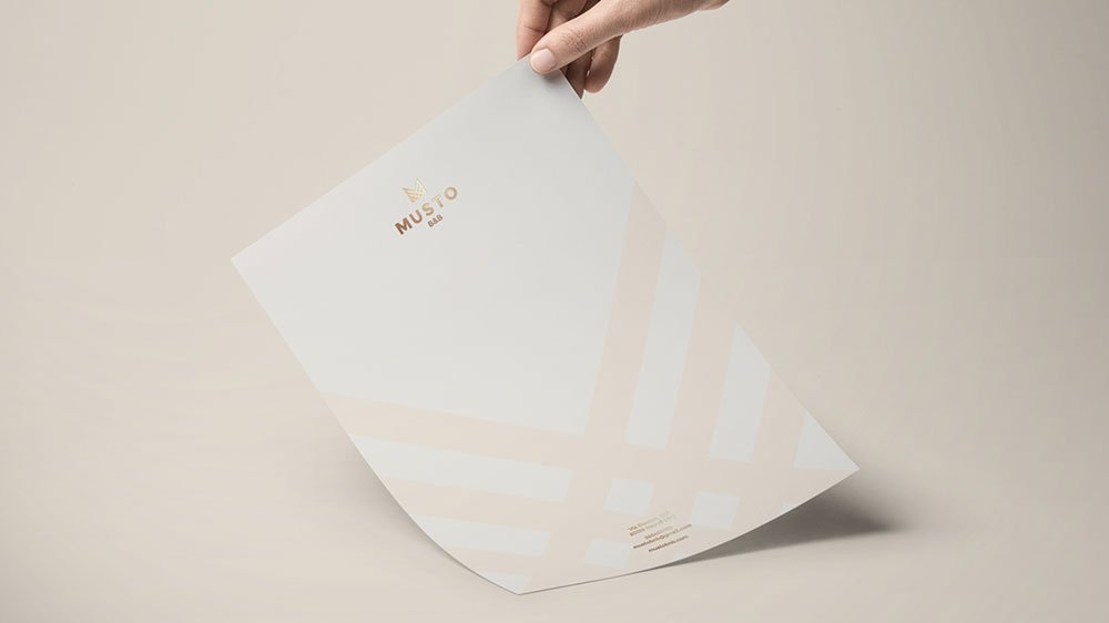 A hand holds a piece of paper with a gold foil Musto logo and pink diagonal stripes