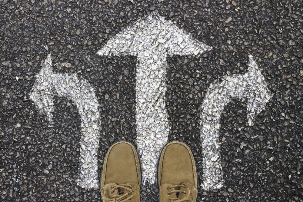 Two feet stood on road in front of white arrows pointing in different directions