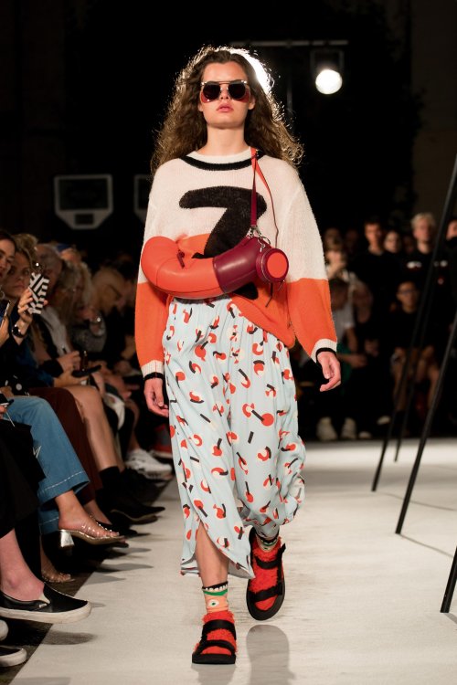 Woman walking down catwalk wearing a patterned blue and orange skirt