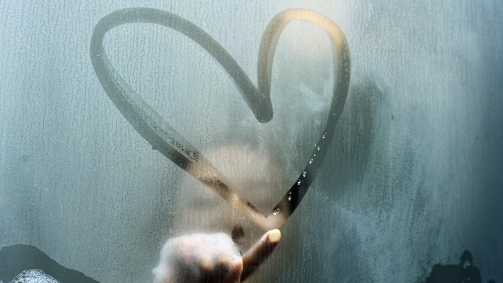 Woman draws heart on misted-up glass