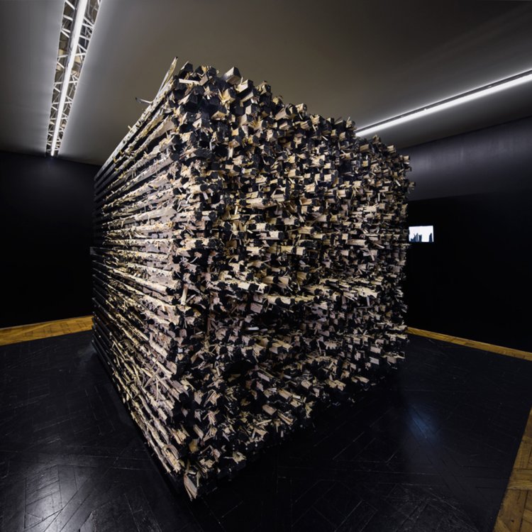 Huge cuboid art installation made of pieces of dark wood, by Akatre